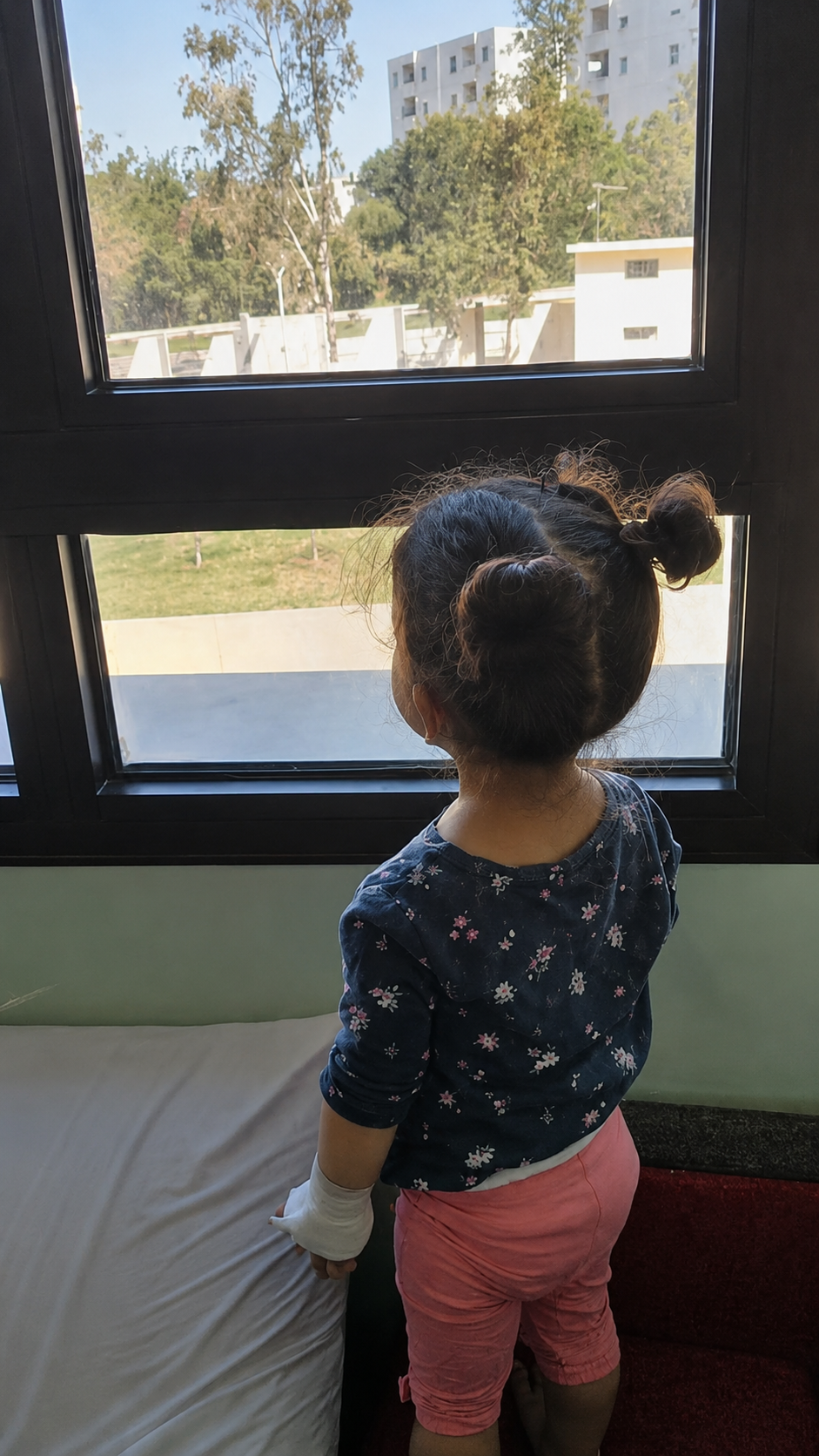 Tasnim regarde les autres enfants jouer à travers les vitres de l’hôpital.